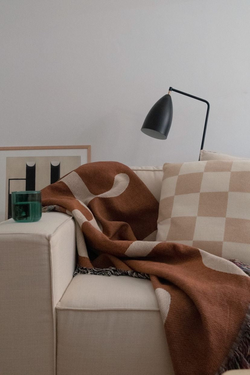 A dimly lit couch with the 'fiesta' mocha clr shop blanket.